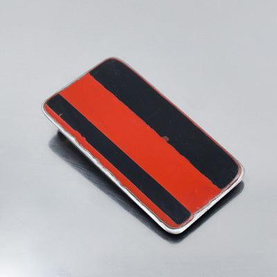 The Ernesto - Dodge Dart is a rectangular metal object with a glossy finish and bold red and black vertical stripes, reminiscent of vintage car parts, shown on a reflective gray background.