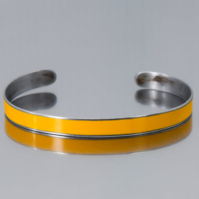 The Norma - Ford pickup is a silver metal cuff bracelet featuring a shiny yellow enamel center stripe inspired by vintage car paint, displayed on a reflective gray surface.