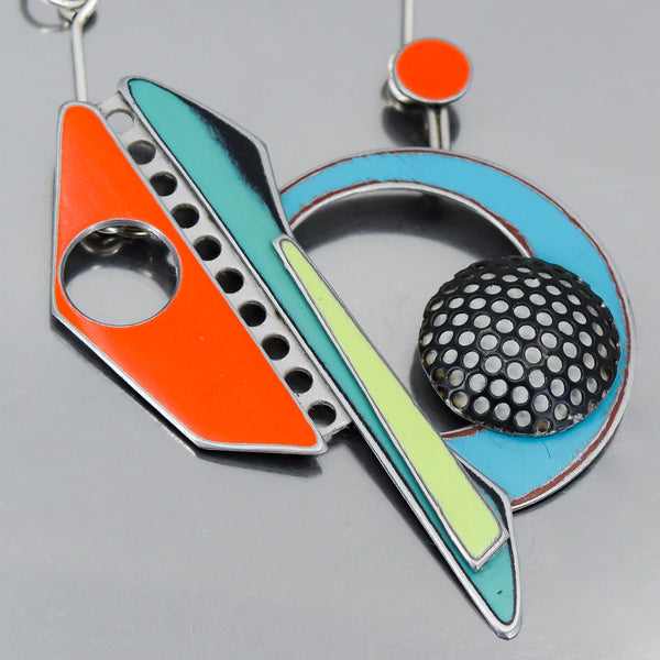 Close-up of a colorful pendant necklace featuring vintage car paint and black perforated metal detailing.