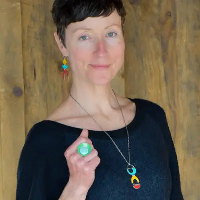 Woman modeling jewelry, wearing a bright, colorful, unique, original ring, necklace and earrings.
handmade using vintage car parts with the original car paint intact. Joyride Jewelry. Jewelry made from vintage car parts. sustainable, recycled