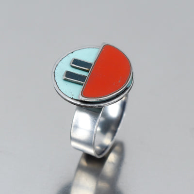 The Myrtle - AMC, Ford, Pontiac ring features a round, flat silver top split in half: one side light blue with two black bars, the other solid red. Vintage car parts and paint inspire its design. Photographed on a reflective gray surface.