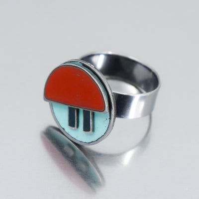 The Myrtle - AMC, Ford, Pontiac is a ring with a round face featuring an abstract design: a red semicircle over light blue and two vertical black rectangles, made from vintage car part.