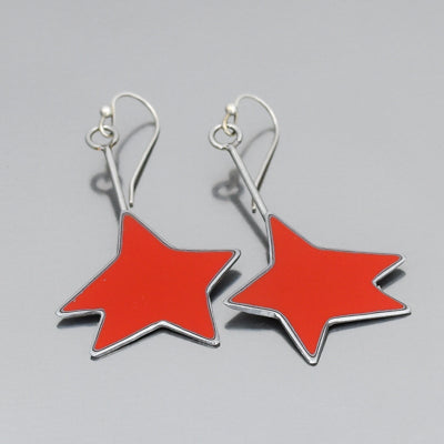 The Hattie - Mercury Monterey earrings feature large red star-shaped pendants with silver outlines and hook fastenings, inspired by vintage car parts with original paint, displayed against a plain gray background.