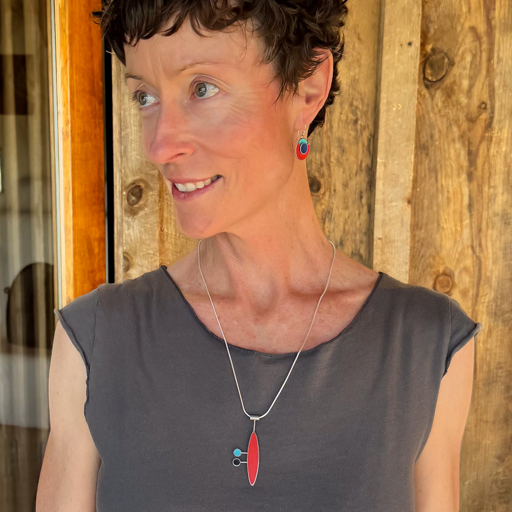 Woman wearing Millie pendant necklace featuring red, turquoise, and black vintage Ford, Mercury, and GMC emblems on sterling silver chain