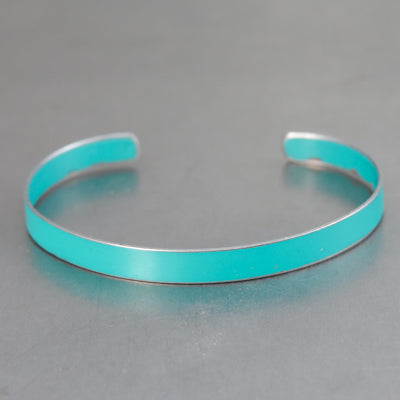 A slim, open-ended turquoise metal cuff bracelet named Jane - Ford Econoline, inspired by vintage car parts with original paint, is displayed on a smooth gray surface.
