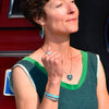 A woman in a green sleeveless top poses confidently wearing matching teal jewelry made from vintage- AMC Rambler car parts, including earrings, necklace, bracelet, and ring, in front of a red  Ford Bronco. Handmade jewelry by Joyride Jewelry.