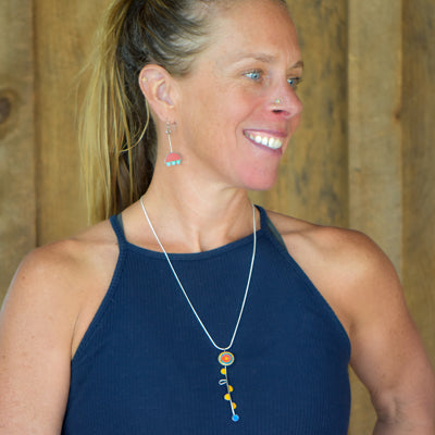 A smiling woman with blond hair in a ponytail wears Wonda - Ford & AMC: a  necklace with a Ford pickup pendant and matching earrings, paired with a navy blue sleeveless top. Free shipping included!.
