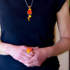A person in a black shirt showcases the Dotty - Ford & Jeep necklace and matching stainless steel ring, both featuring orange and yellow circular designs. Their clasped hands at waist level draw attention to the vibrant jewelry.