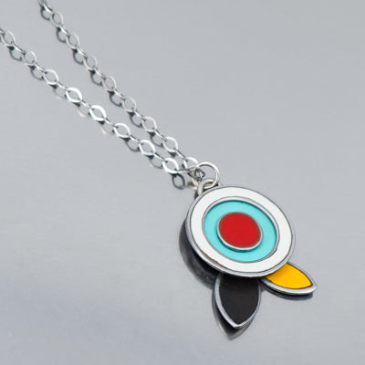 The Fannie - Ford, Dodge, Oldsmobile necklace features a silver chain with modern concentric circles in white, turquoise, and red above three teardrop shapes, all set against a smooth reflective background.