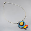 The Verna - Ford & Mercury is a silver necklace on a sterling cable featuring a stylized fish pendant with concentric blue, yellow, and purple circles, plus orange, yellow, and white teardrop fins. Pendant dimensions available upon request.