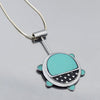 The Gertrude - Chevy & Ford is a necklace with a turtle-shaped pendant featuring turquoise enamel, white polka dots on black, and a minimalist design on a sleek sterling silver chain made from vintage car parts by Joyride Jewelry.