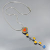 The Wonda - Ford & AMC necklace features a circular blue, orange, and yellow pendant with a curved bar accented by four yellow-orange triangles and a blue circle on a sterling silver chain. Reminiscent of a flower this is a handmade original design by Joyride Jewelry made from vintage car parts. 
