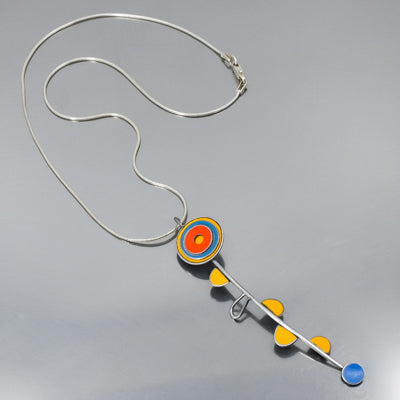 The Wonda - Ford & AMC necklace features a circular blue, orange, and yellow pendant with a curved bar accented by four yellow-orange triangles and a blue circle on a sterling silver chain. Reminiscent of a flower this is a handmade original design by Joyride Jewelry made from vintage car parts. 