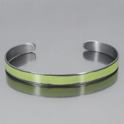 The Oliver-Plymouth Satellite is a sleek, metallic adjustable bracelet featuring a smooth light green enamel strip at the center, shown on a reflective gray surface. Enjoy free shipping on this elegant accessory.