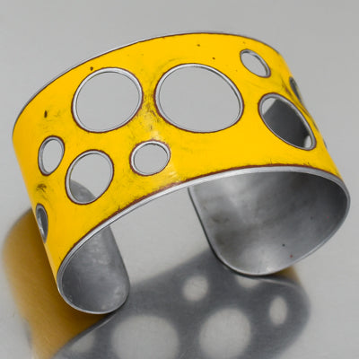 The Ira - Ford pickup is a wide yellow metal cuff bracelet with circular cutouts in various sizes and a lightly distressed finish, made from vintage car parts. 