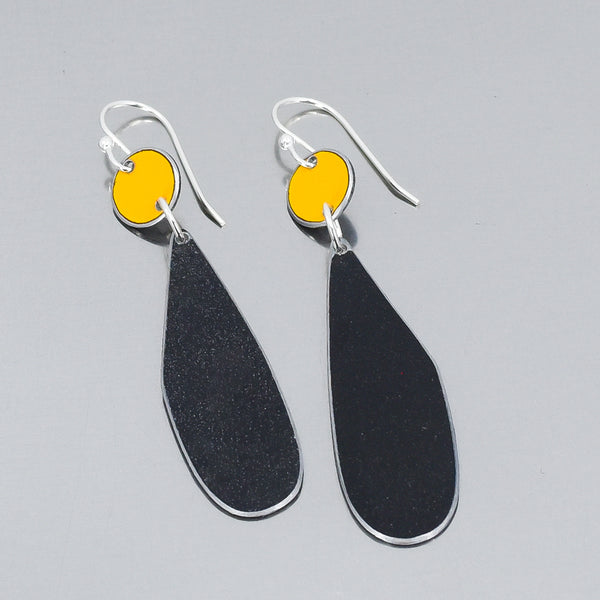 Silver earrings with yellow circular tops and elongated black teardrop metal pieces from vintage trucks