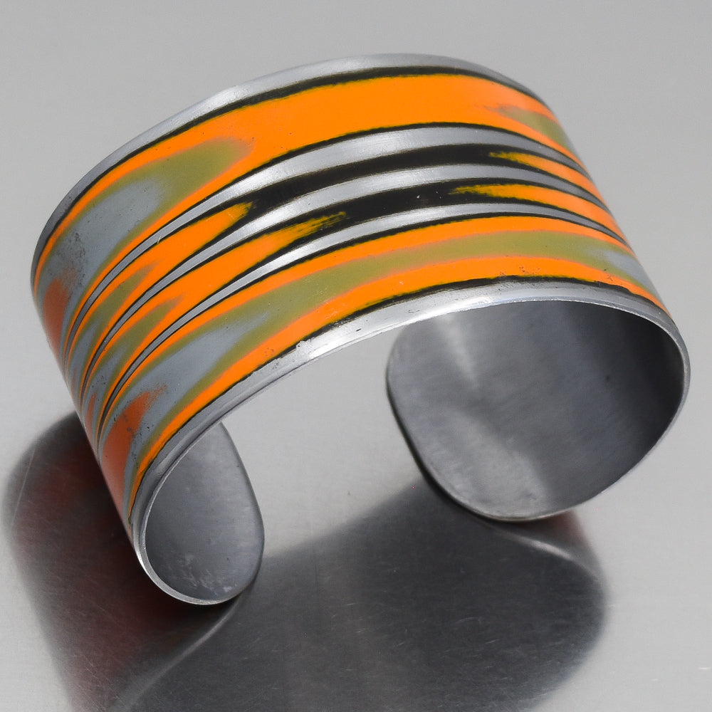 Adjustable cuff bracelet made from 1979 International Scout with original orange car paint intact, shown on metal surface.
