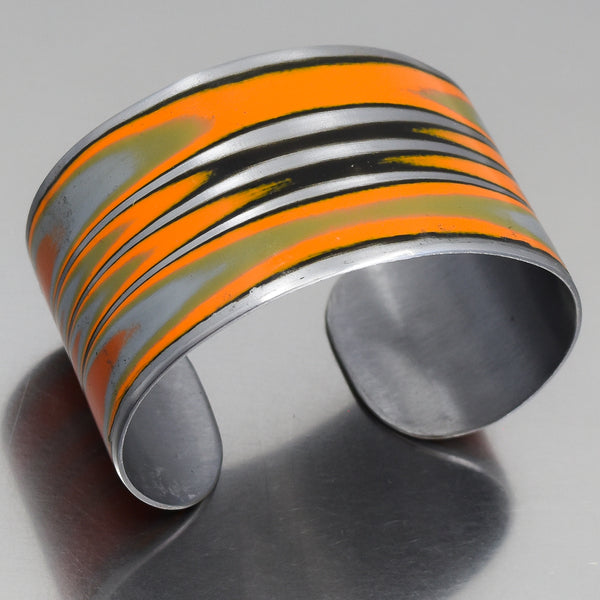 Adjustable cuff bracelet made from 1979 International Scout with original orange car paint intact, shown on metal surface.