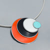 The Lenora - Ford & Dodge necklace features a modern pendant with overlapping turquoise, white, black, and orange enamel layers on a sterling silver cable and thin silver chain.