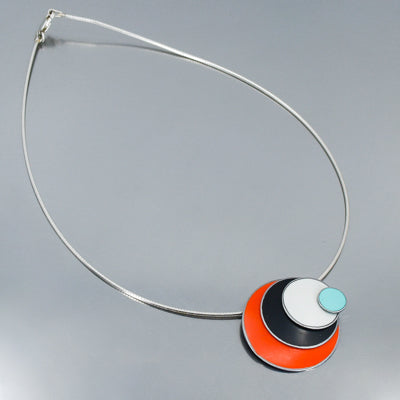 The Lenora - Ford & Dodge necklace features a modern pendant with overlapping turquoise, white, black, and orange circles on a sleek sterling silver cable in a layered, geometric design.
