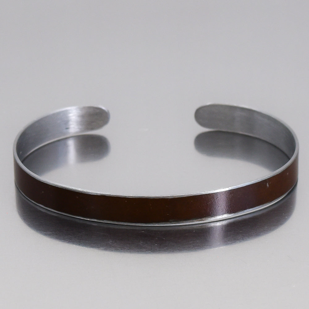 Close-up of a silver cuff bracelet with a brown Oldsmobile painted steel inlay named Marvin on a reflective surface
