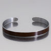 Close-up of a silver cuff bracelet with a brown Oldsmobile painted steel inlay named Marvin on a reflective surface