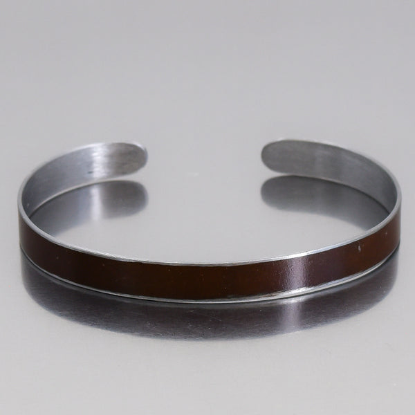 Close-up of a silver cuff bracelet with a brown Oldsmobile painted steel inlay named Marvin on a reflective surface