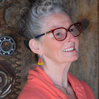 Jean - Mazda & Dodge earrings worn by woman with gray hair and red glasses against rustic wooden background