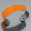 The Norbert - AMC Rambler is a bright orange metal bracelet made from a 1960 AMC Rambler with the original car paint intact, featuring a thin etched line down the middle. 