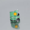 The Lee - Dodge & Ford is a modern silver ring with a glossy mint green enamel, inspired by classic car paint, and features a bold yellow circle highlighted by a central clear gemstone, shown on a reflective grey surface.