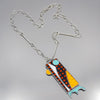 Gracie - Ford & Dodge: A silver chain necklace with a colorful, abstract fish-shaped pendant made from salvaged automotive materials in orange, black, blue, and white geometric patterns. Displayed on light gray. Free shipping!.