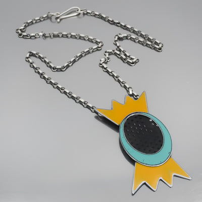 The Wonda - Datsun & Chevy is a silver chain necklace featuring a stylized candy pendant with a turquoise oval center, black dots, and pointed yellow ends, hanging from an oxidized sterling silver chain on a gray background.