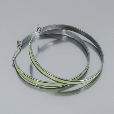 Claire - Plymouth Satellite: Large silver hoop earrings with stainless steel ear wires and a thin light green center stripe, displayed on a light gray surface.