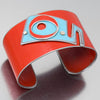 The Emmett - Ford is a wide, red metal adjustable bracelet featuring a raised abstract geometric design in light blue and silver with a central red circle, Made by vintage Ford Fairlane parts displayed on a reflective surface.