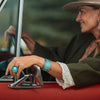 A smiling woman in a hat and green jacket sits in the driver’s seat of  a 74 Ford Bronco wearing the Frankie cuff bracelet and a ring. Each piece is made from vintage cars with the original car paint intact.