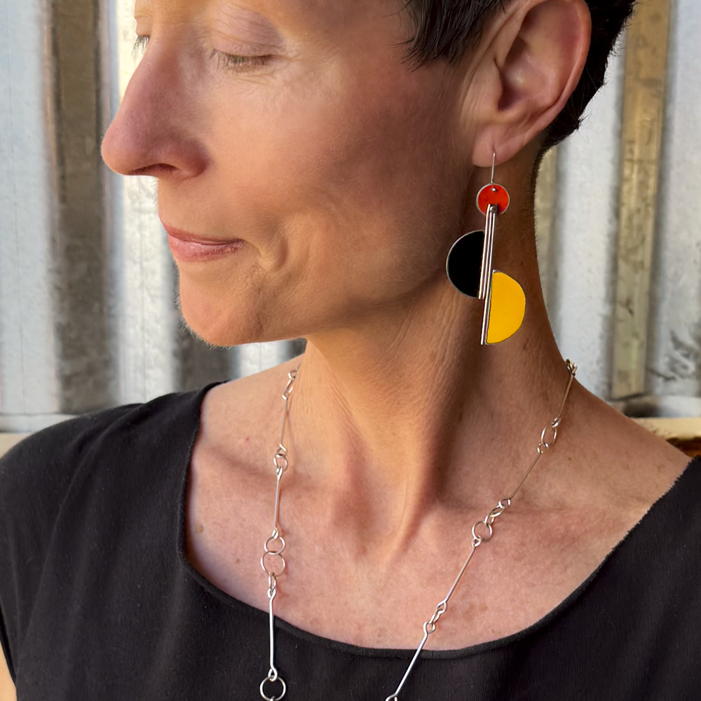 Close-up of a woman wearing Ollie - Ford & GMC earrings with orange, black, and yellow original car paint accents.