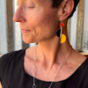 Close-up of a woman wearing Ollie - Ford & GMC earrings with orange, black, and yellow original car paint accents.