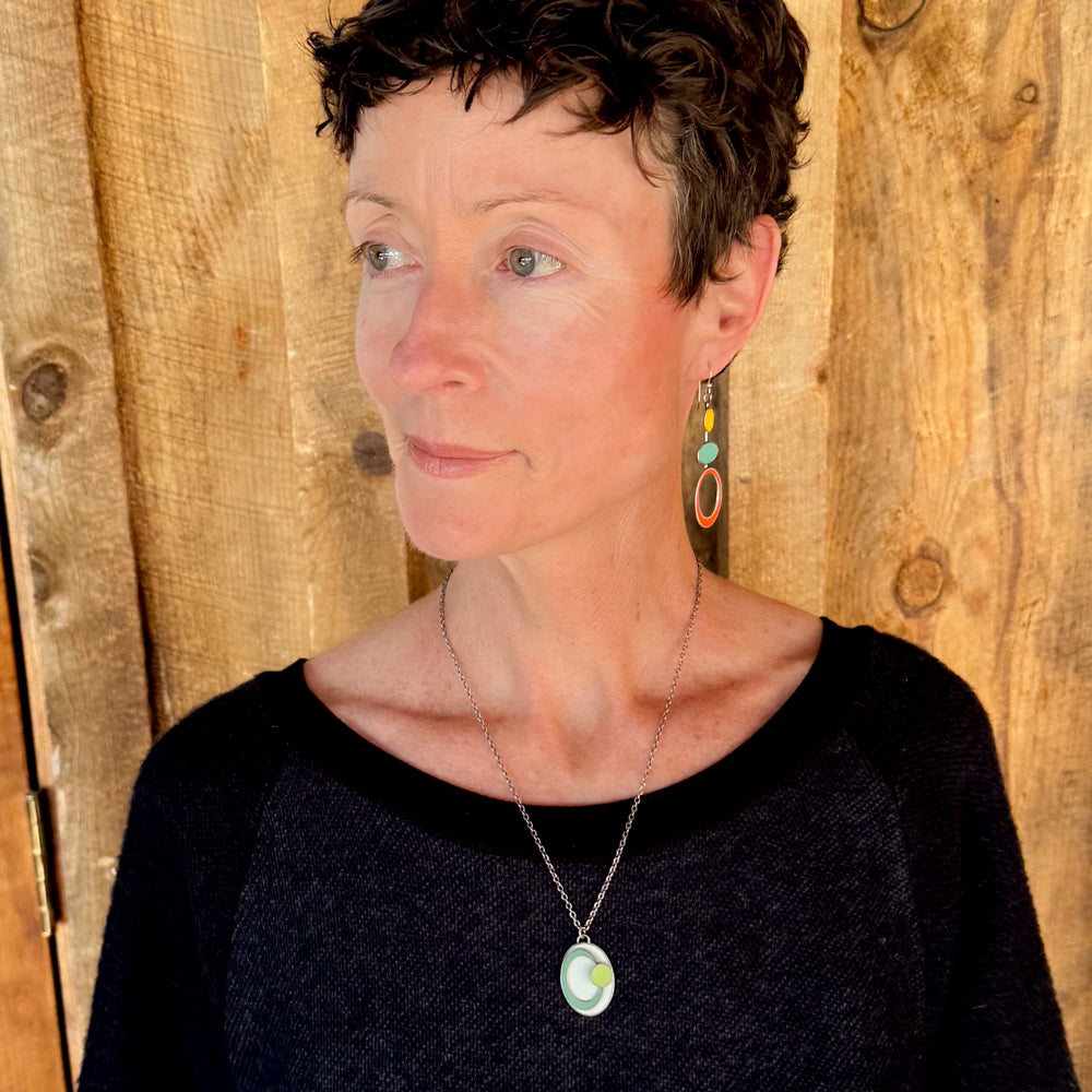 Woman modeling jewelry, wearing a bright, colorful, unique, original necklace and earrings.
handmade using vintage car parts with the original car paint intact. Joyride Jewelry. Jewelry made from vintage car parts. sustainable, recycled 

