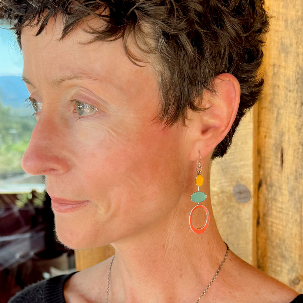 Woman modeling jewelry, wearing a bright, colorful, unique, original necklace and earrings.
handmade using vintage car parts with the original car paint intact. Joyride Jewelry. Jewelry made from vintage car parts. sustainable, recycled 

