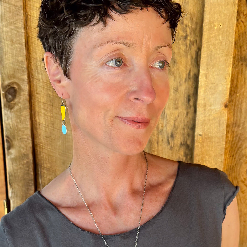 Woman modeling jewelry, wearing a bright, colorful, unique, original necklace and earrings.
handmade using vintage car parts with the original car paint intact. Joyride Jewelry. Jewelry made from vintage car parts. sustainable, recycled 

