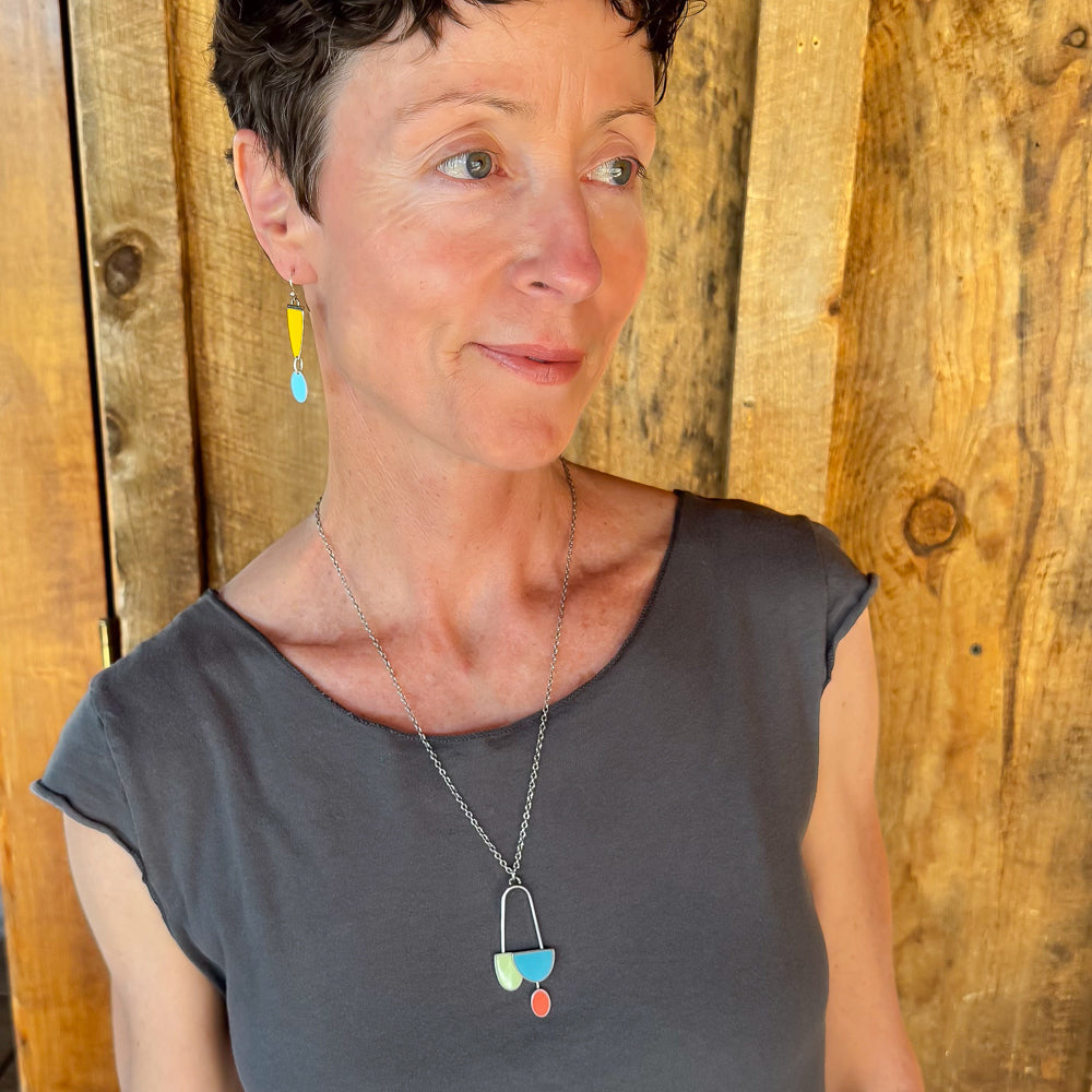 Woman modeling jewelry, wearing a bright, colorful, unique, original necklace and earrings.
handmade using vintage car parts with the original car paint intact. Joyride Jewelry. Jewelry made from vintage car parts. sustainable, recycled 

