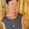 Woman modeling jewelry, wearing a bright, colorful, unique, original necklace and earrings.
handmade using vintage car parts with the original car paint intact. Joyride Jewelry. Jewelry made from vintage car parts. sustainable, recycled 

