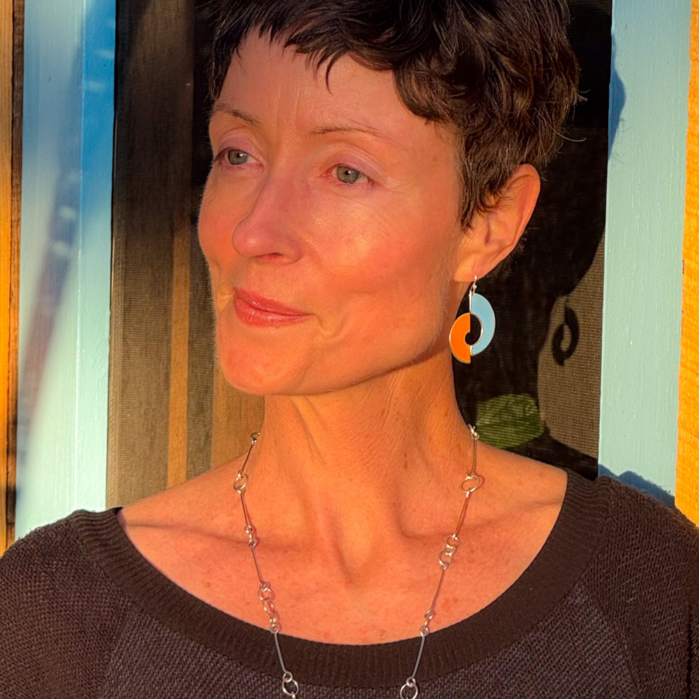 Woman wearing Sterling silver ear wire earrings with orange and blue International Scout car paint design