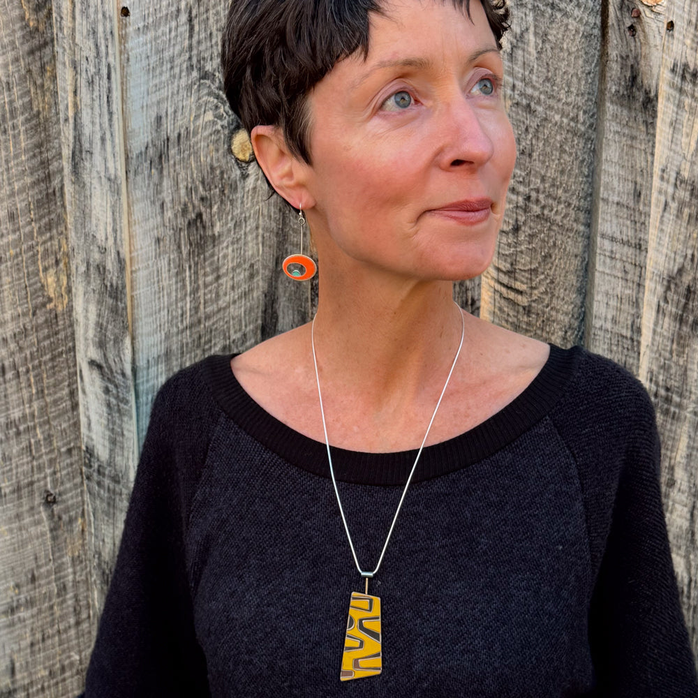 Woman wearing a sterling silver snake chain necklace with a yellow Ford pickup pendant and an orange earring.