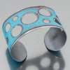The Ira - Ford Thunderbird is a wide, silver adjustable bracelet featuring a turquoise surface with circular cutouts and a distressed finish, inspired by original 1964 Ford Thunderbird car paint.
