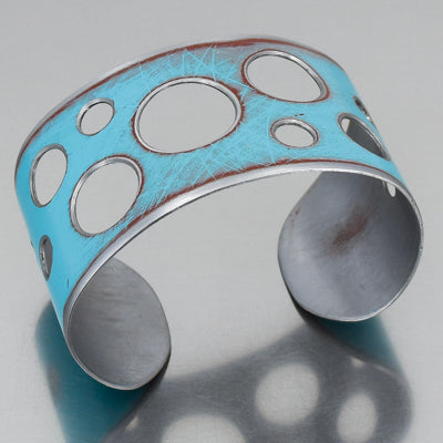 The Ira - Ford Thunderbird is a wide, silver adjustable bracelet featuring a turquoise surface with circular cutouts and a distressed finish, inspired by original 1964 Ford Thunderbird car paint.