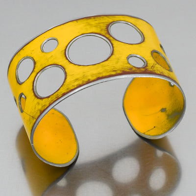 The Ira - Ford pickup is a wide yellow cuff bracelet with multiple circular cutouts of varying sizes. Made using vintage car parts with the original car paint intact. Handmade jewelry by Joyride Jewelry.