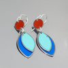 The Willa - Mercury, AMC, Dodge earrings feature red circular tops and layered light blue and dark blue leaf-shaped pendants in silver-tone metal, reminiscent of vintage car parts with original paint, shown on a gray background.