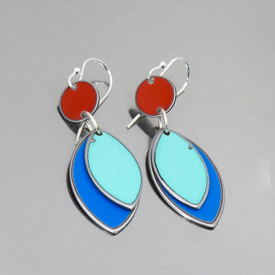 The Willa - Mercury, AMC, Dodge dangle earrings feature red circular tops and layered leaf-shaped pendants in light and royal blue with silver outlines, made from  classic car parts, displayed on a gray background.