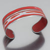 The Wilson - Jeep Willys is a silver adjustable bracelet with a red and white abstract stripe design, inspired by the original paint of the Jeep Willys station wagon, shown on a reflective gray surface.